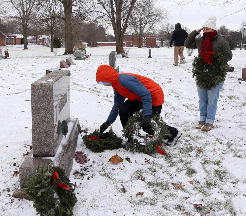 Benjamin Carter of Yorkville places a wreath while Navy Veteran Joanne Gabl of Elburn salutes at St. Gall’s Cemetery in Elburn on Saturday, Dec. 17, 2022.