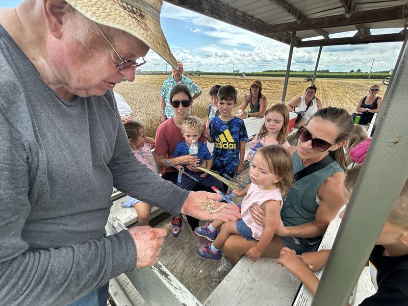 Roger Mixer of East Moline, shows kids how wheat is gleaned as a combine harvests a field in the background during a tour at the Bos Brothers Historical Farm south of Erie on Friday, July 25, 2025.