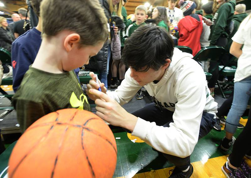 Glenbard West state basketball player Bobby Durkin signs t-shirts and basketballs for children including John Hall during the pep rally held Sunday March 13, 2022.