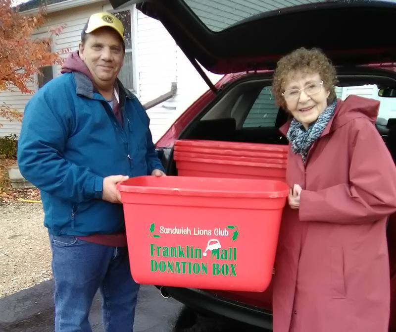 Pat Wallis (right) and Lion Kyle Wallis (left), daughter and grandson of the late Franklin Mall, are shown preparing the red collection bins which are now in place throughout the community to receive donations of non-perishable food items for the annual Sandwich Lions Club Franklin Mall Christmas Food Project.  The Wallises, along with other family members, have been instrumental in helping to keep the tradition of this project going for over 60 years.