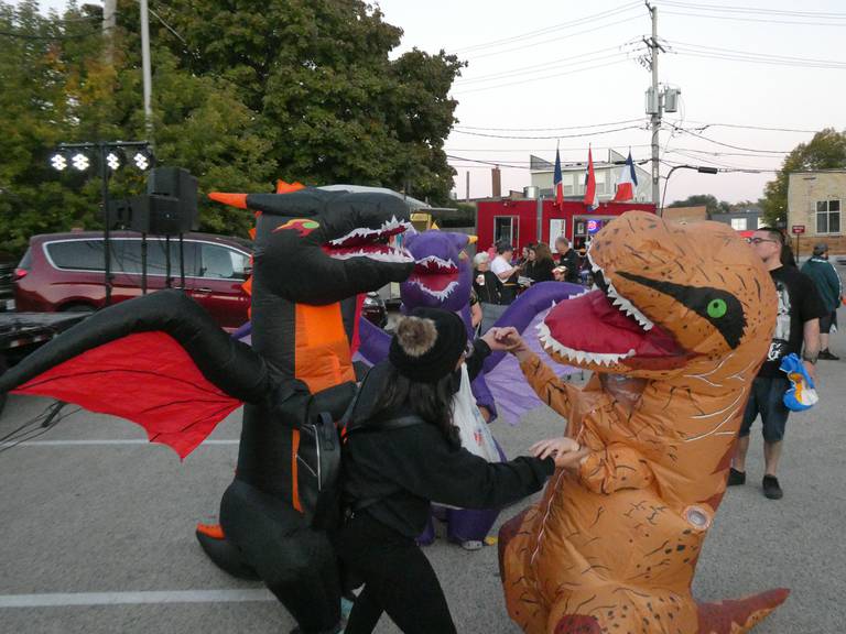 A dinosaur and two dragons dance to the music during Green Street Cruise Night's Halloween Special in McHenry on Monday, Oct. 10, 2022. Parents at the event said that these types of inflatable costumes have become more prevalent over the past few years.