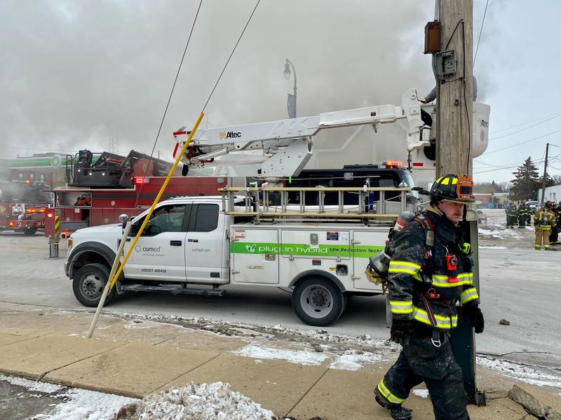 A DeKalb firefighter walks past a ComEd truck as a ComEd worker is lifted to a power line across the street of a working fire at a two-story duplex on Saturday, Jan. 24, 2026, at Seventh Street and East Lincoln Highway in downtown DeKalb. More than a dozen first responders battled not just the fire but frigid cold, as temperatures had dropped to single digits with subzero wind chills.