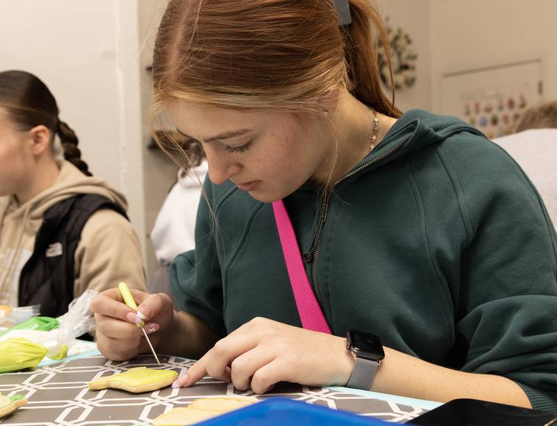 Lilia Muffler uses a sugar-stiring needle Thursday, March 16, 2023, as she decorates a leprechaun hat during a cookie decorating class. "It takes a lot longer than they show (online). They make it look easy but it's a lot harder."