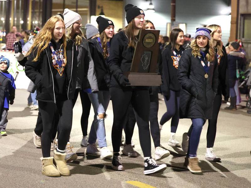 The state champion Genoa-Kingston volleyball team carry their trophy through downtown in 21st Annual Jingle Bell Walking Parade Friday, Dec. 2, 2022, during Celebrate the Season hosted by the Genoa Area Chamber of Commerce.