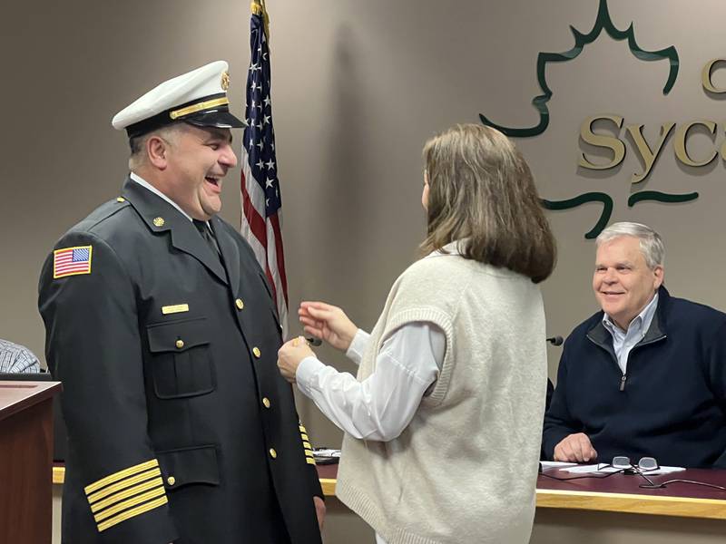 Sycamore Mayor, Steve Braser, right, looks on as Carl Reina, left, smiles while his wife, Kelly Reina, middle, pins the Sycamore fire chief badge on Jan. 18, 2023, when Carl Reina was sworn-in as the city of Sycamore's newest fire chief.