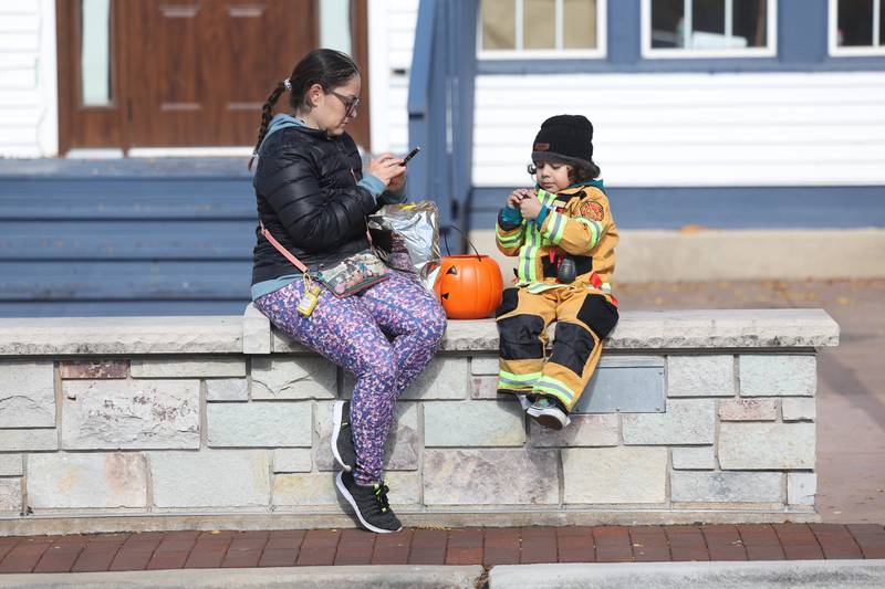 Diana Silva checks her messages while her 5-year old son Antonio eats candy as they take a break at the annual Halloween Spooktacular in downtown Plainfield on Saturday, Oct. 28, 2023.