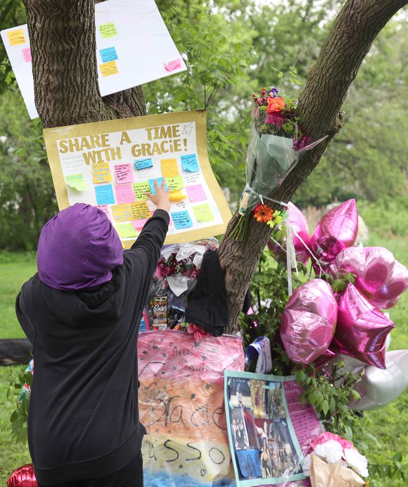 Layla Jones moves a sign filled with messages as rain begins to fall during a memorial for slain teen Gracie Sasso-Cleveland Friday, May 12, 2023, behind a building in the 500 block of College Avenue in DeKalb.