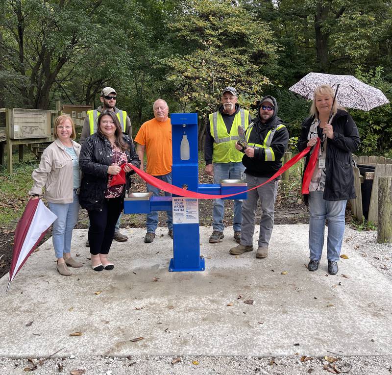 Ellen Vogel of Live Well Streator (left), Mayor Tara Bedei and Holly Howard of Illinois American Water pose for a ceremonial ribbon cutting photo Friday, Oct. 6, 2023, with Streator Public Works staff to dedicate a new bi-level drinking fountain at Spring Lake Nature Park.