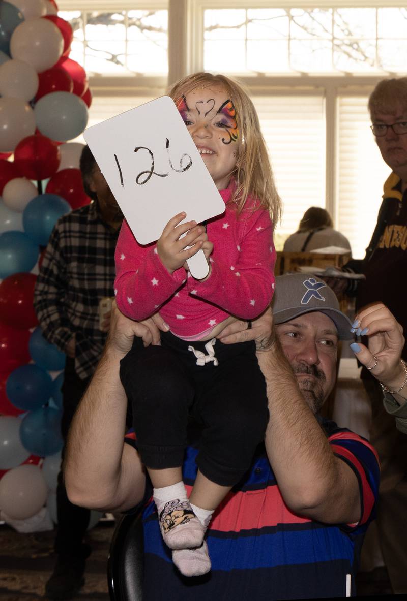 Emma Meseke, 3, of Ottawa helps hold up a paddle making the winning bid during the live auction Sunday, April 21, 2024, at Senica's Oak Ridge in La Salle during the Chocolate Festival fundraiser benefitting La Salle County Court Appointed Special Advocates.