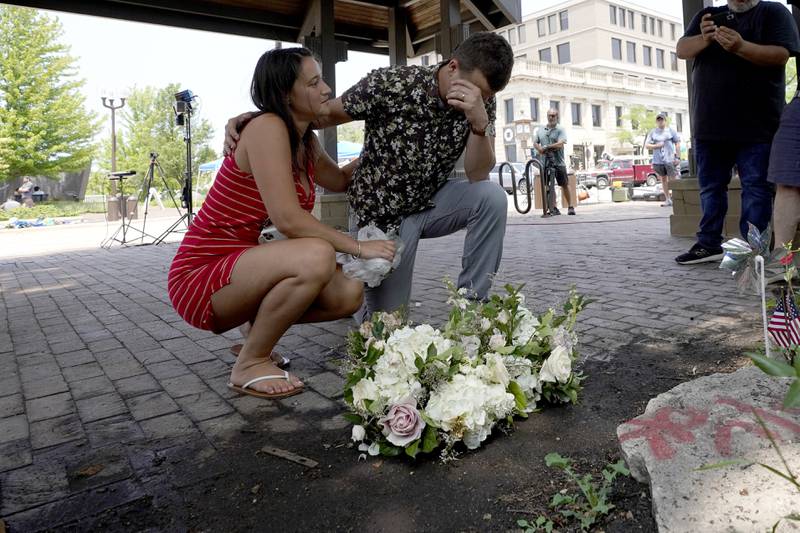 Brooke and Matt Strauss, who were married Sunday, pause after leaving their wedding bouquets in downtown Highland Park, Ill., near the scene of Monday's mass shooting Tuesday, July 5, 2022, in Highland Park, Ill. (AP Photo/Charles Rex Arbogast)
