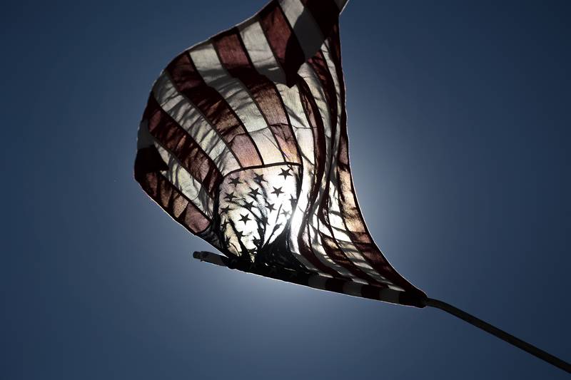 The morning sun shines through a flag placed along the route the traveling Vietnam Traveling Memorial Wall will use as it comes in to Rock Falls Thursday, August 31, 2023.