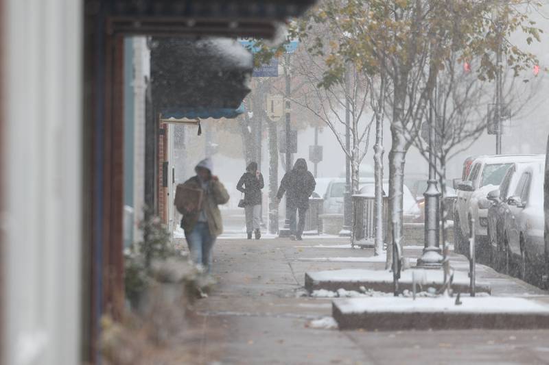 People along West Lockport Street in downtown Plainfield during the first snowfall of the season on Thursday, Nov. 21, 2024.on Thursday, Nov. 21, 2024.