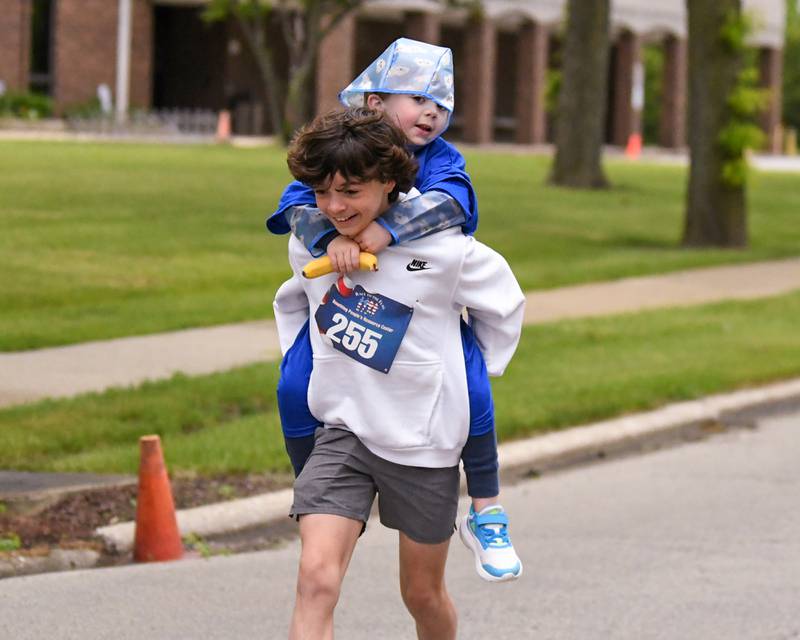 Ashton Collins, 13, of Westmont runs with Chase Collins, 4, on his back during the Race to the Flag 5k on Sunday May 25, 2025, held at Ty Warner Park in Westmont.