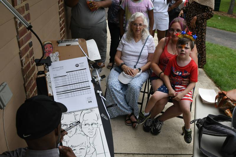 (From left) DeKalb family members Gale Holladay, Emilyn Ritchie and Elliott Land, 6, get a caricature done during the Fourth of July celebration held at Hopkins Park in DeKalb on Thursday, July 4, 2024.