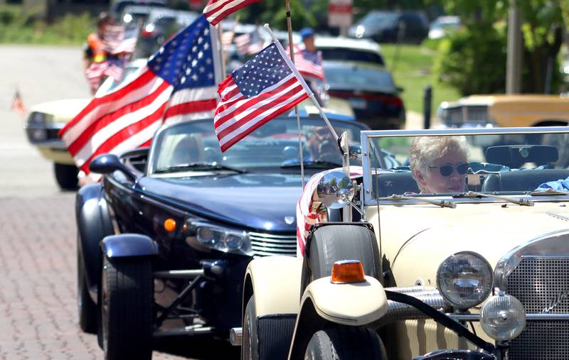 Classic vehicles cruise with flags during a Memorial Day  parade in downtown Woodstock on Monday, May 26, 2025.