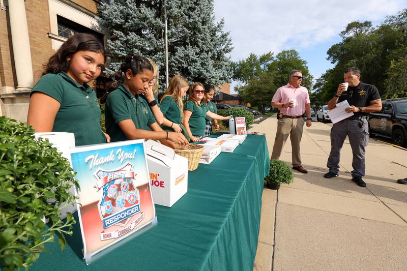 Bishop McNamara Catholic School fifth graders prepare to offer coffee and donuts as they host the 10th Gratitude Drive-Thru for first responders and military members on Thursday, Sept. 11, 2025. Kankakee County Undersheriff Chad Gessner and Bradley Police Lt. Robert Mason enjoy coffee in the background.