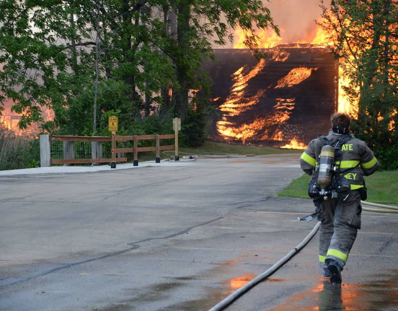A firefighter runs with a hose Monday, May 30, 2022, toward a cabin unit on fire at Grand Bear Resort in Utica.