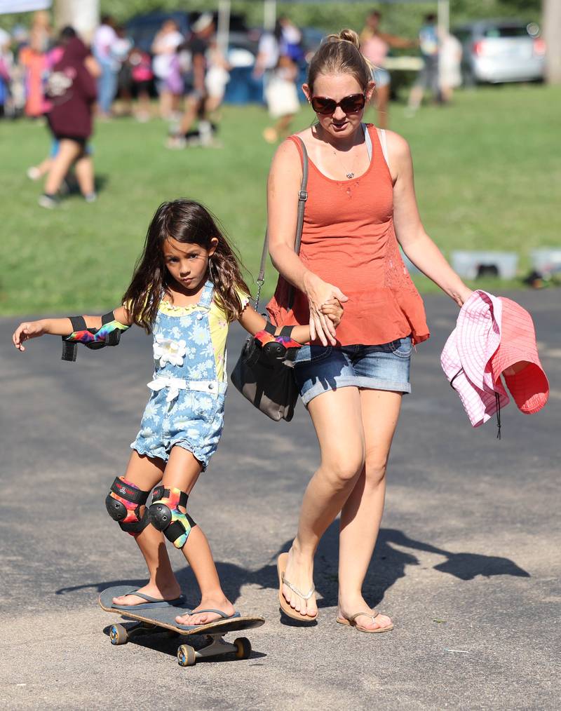 Evelyn Pineda, 6, from DeKalb, gets a hand from her mom Jennifer while trying to skateboard at the Pushing Together/Fargo Skateboard booth during the Family Fun Fest Thursday, July 20, 2023, at Hopkins Park in DeKalb.