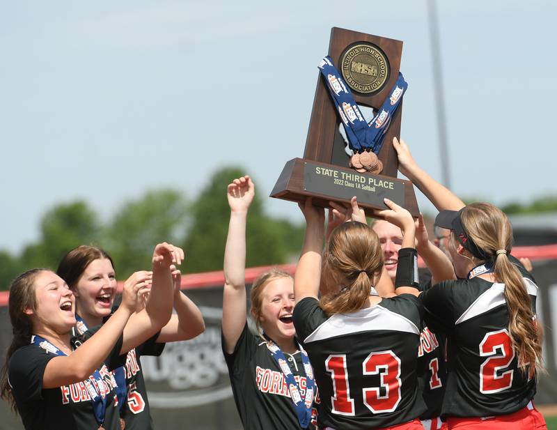 Forreston seniors Kara Erdmann (13) and Breanna Kloster (24) show the third place trophy to their teammates after beating Newark 4-2 in 8 innings at the 1A state softball finals in Peoria on Saturday.
