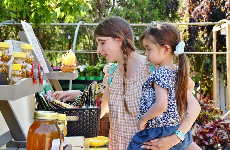 Ariel Shiota of Sycamore holds her daughter, 4-year-old Guinevere, as they shop at Little Red Truck Apiary's stand at the Sycamore farmers market Tuesday.