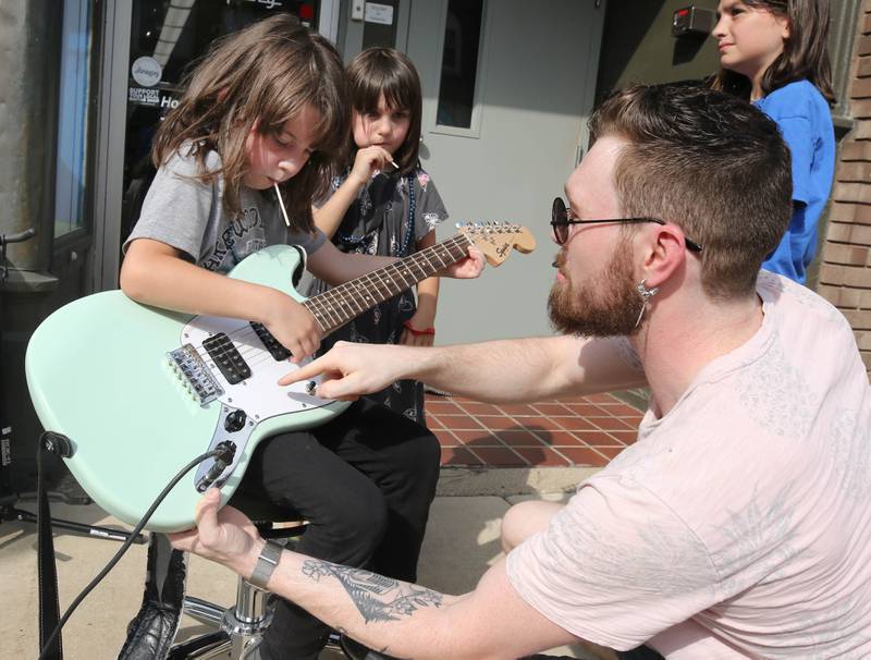 Lilly Bildusas, 7, from DeKalb, gets a lesson from Connor Murray, from the Aurora Music Company, in front of their store at Corn Fest Friday, Aug. 25, 2023, in downtown DeKalb.