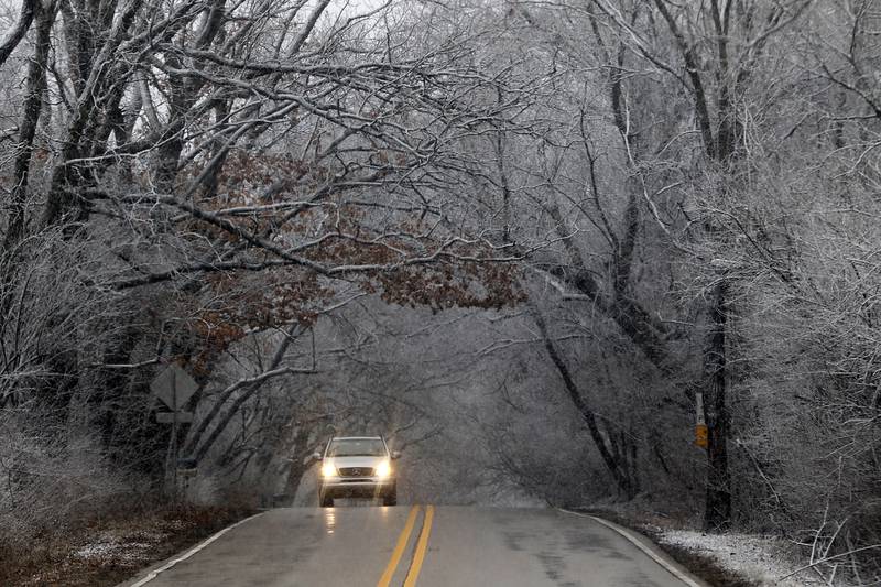 Snow sticks to the trees as a motorist drives west on Bull Valley Road towards North Fleming Road on Thursday, March 31, 2022. Areas of McHenry County faced a day of rain and snow showers.