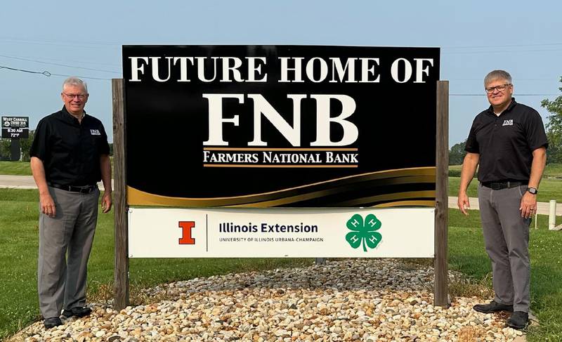 Garett Plumley, President/CEO of FNB (left) and Bart Ottens, Mt Carroll Community Bank President (right) pose by the sign announcing the future home of a FNB branch in Mount Carroll.