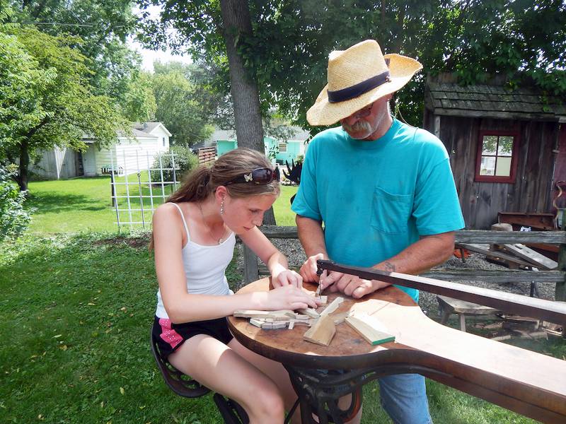 Volunteer Gary Eggleston of Genoa helps Elizabeth Melton, 10, of Sycamore as she cuts a piece of wood with a pedal-powered scroll saw Sunday at the Kishwaukee Valley Heritage Society's Pioneer Day festival.
