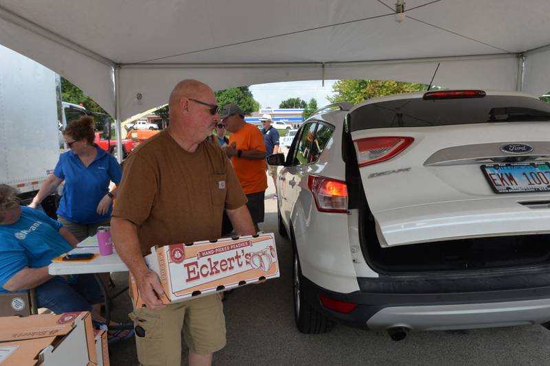 Dixon Kiwanian Don Knight carries a box of peaches to a vehicle during the club's distribution day in a Dixon High School parking lot on Thursday, Aug. 10, 2023.
