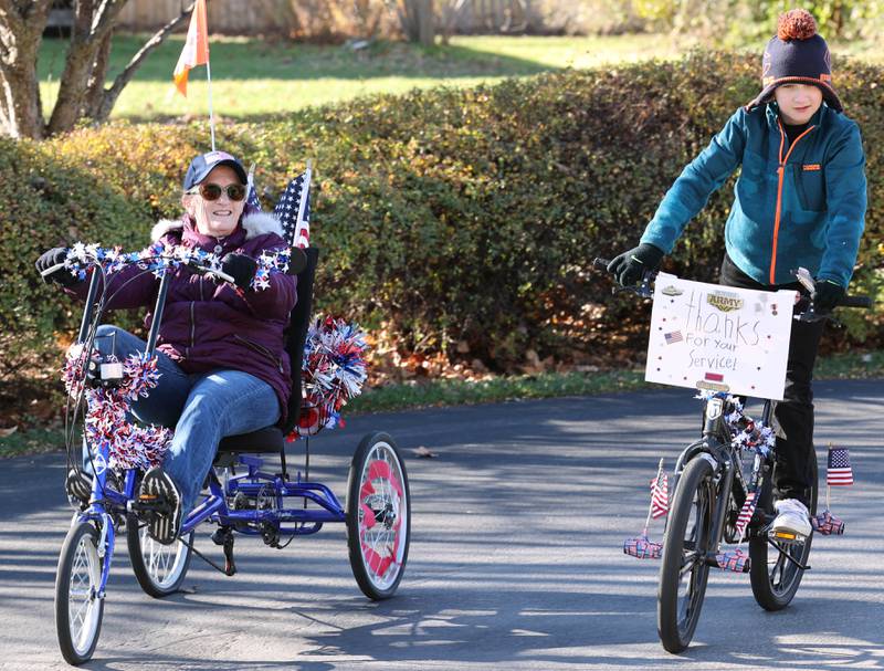 Joann Kunkel, from Sycamore, and her grandson Jameson, 9, ride in a small parade with other family members on Veterans Day, Friday, Nov. 11, 2022, for the veterans at the Grand Victorian assisted living facility in Sycamore. Joann Kunkel read a story in the Midweek that contained a quote from one of the veterans at the facility that lamented the lack of a parade. So she and her grandkids decided to have one for them.