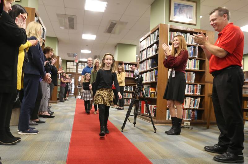 Author Reese Carney 8, of Utica walks down a red carpet with her father Pat, mother Emily and sister Avery, in McCormack Memorial Library to release her new book titled "Reeses Fantastic Surgery Adventure" on Monday, Nov. 6, 2023 at La Salle-Peru Township High School.