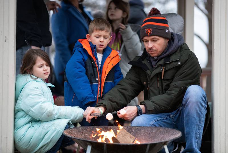 Sam Borah, right, helps his kids Archer Borah, (4) middle, and Rowan Borah (6) roast marshmallows during a Merry & Bright Victorian Christmas at the Downers Grove Museum on Saturday, Dec. 14, 2024.