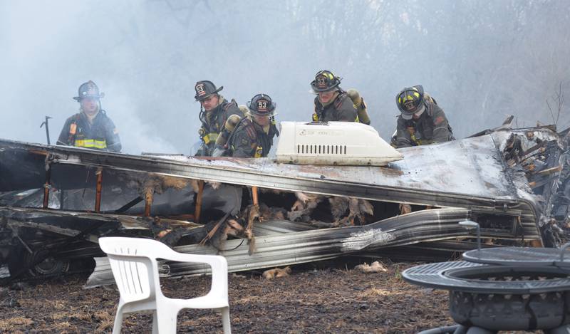 Firefighters look for hot spots in a charred and collapsed recreational vehicle during a garage fire at 6727 W. Henry Road, southeast of Polo, on Wednesday, March 26, 2025. Several departments responded to the fire at the rural residence.