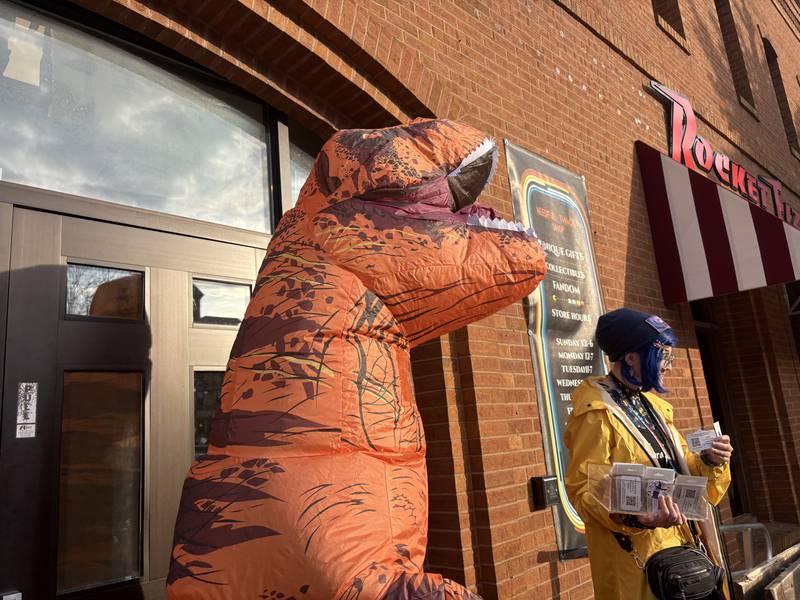 Courtney Dienhart, right, is joined by a person in a dinosaur costume during Halloween on the Square in Woodstock Oct. 31, 2025.