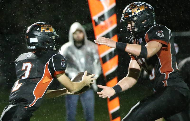 Flanagan-Cornell/Woodland quarterback Seth Jones (2) hands the ball off to Kesler Collins (55) against South Beloit during the first round of the eight-man football playoffs Friday, Oct. 27, 2023, in Flanagan.