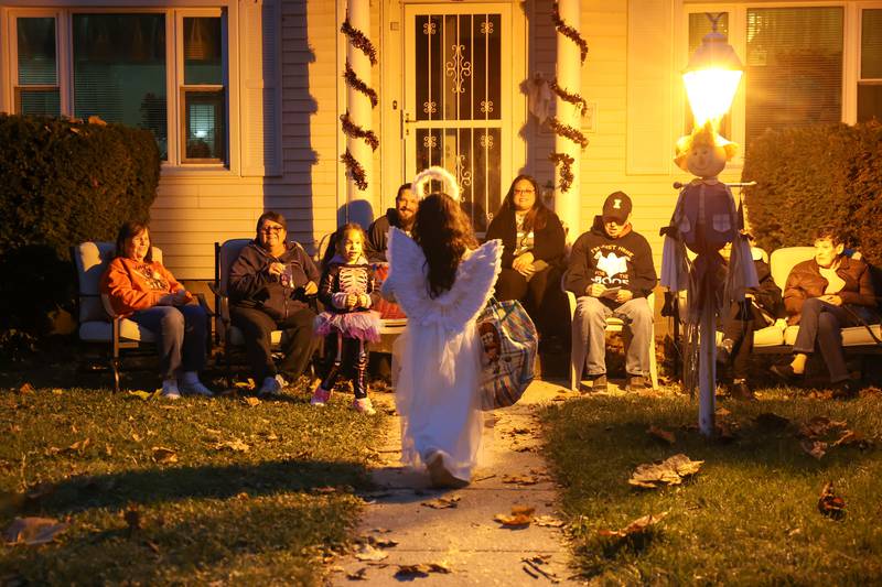 A child dressed as an angel approaches the Bradley home of Jean Tanner, left, as her neighbor, Madonna Bertrand, second from left, gather with friends and family to greet trick-or-treaters on Friday, Oct. 31, 2025.