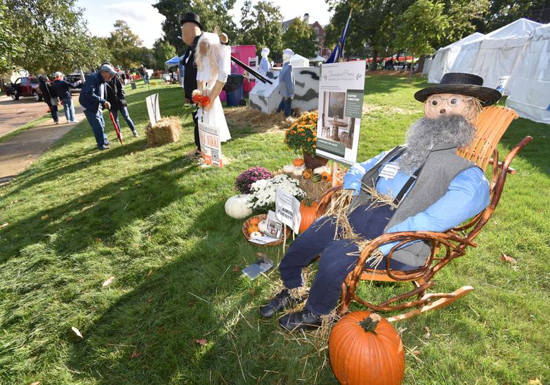 Visitors look closer at a bride and groom scarecrow as another, sponsored by Amish Firniture store sits in a wooden rocking chair at the Annual Scarecrow Festival in Lincoln Park in St. Charles on Friday, October 6, 2023. The event runs through the weekend with family activities and a chance to vote for your favorite scarecrow.