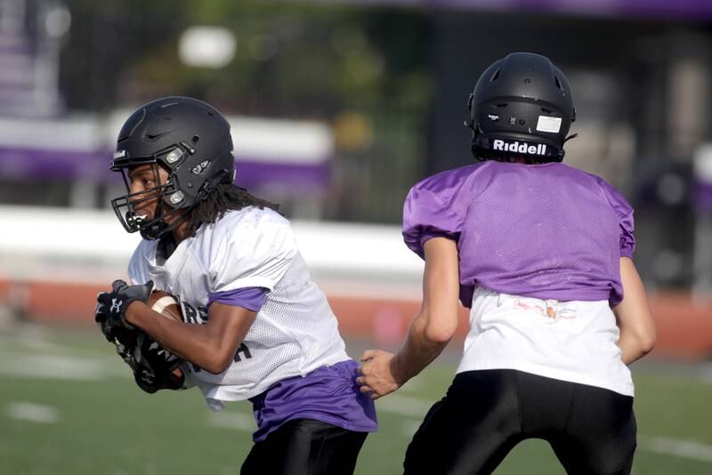 Downers Grove North’s James Lumpkin gets the hand-off from quarterback Owen Lansu during a practice at the school on Tuesday, Aug. 15, 2023.
