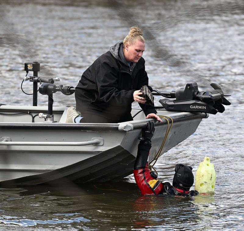 Diver Mike McFerron handed debris, believed to be from a submerged car in the Fox River, to Lindsay Bussick of Chaos Divers on Monday. They were searching for clues related to a cold case from 1983 that the Elgin Police Department is investigating.