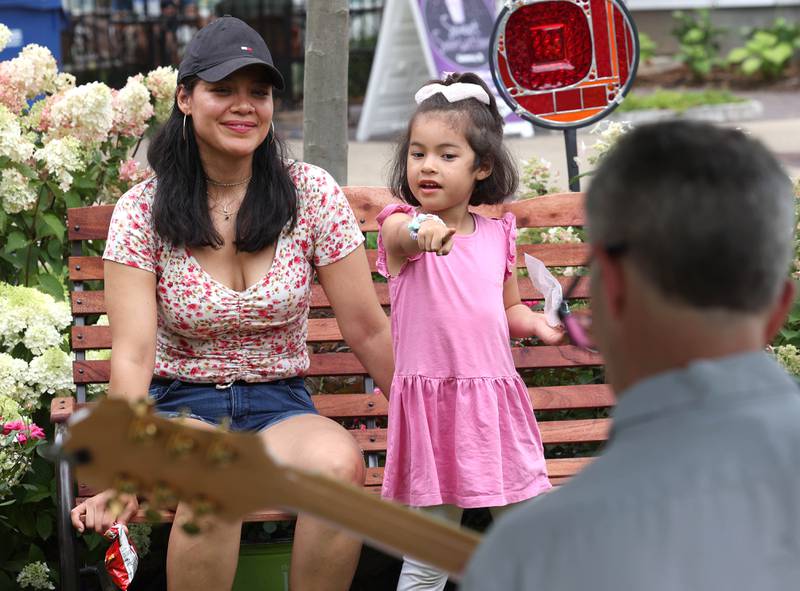 Luz Corona and her daughter Leilah, 4, from Aurora, listen to a musician in the Plandscape area Saturday, July 26, 2025, during the Geneva Arts Fair on third street in Geneva.