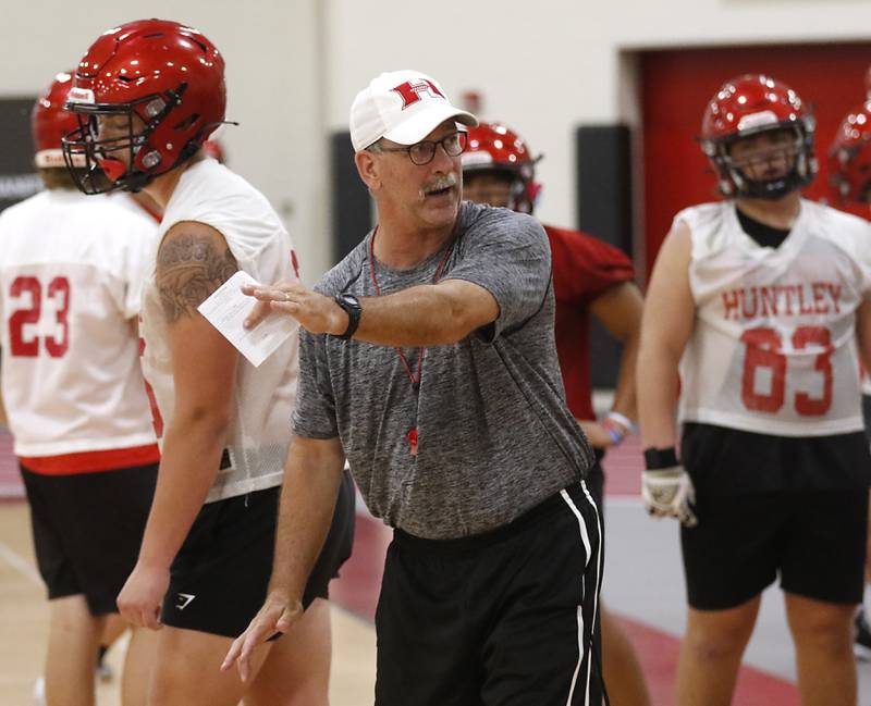 Huntley Offensive coordinator Mike Slattery explains a blocking assignment during the first day of football practice Monday, 8, 2022, in the Huntley High School  field house after stormy weather move practice inside.