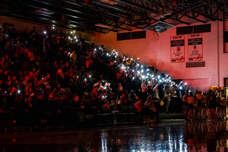 Joliet West fans hold up the flashlights on their cellphones  during the announcement of their starting lineup against Plainfield South  Tuesday Feb. 14, 2023 at Joliet West  High School