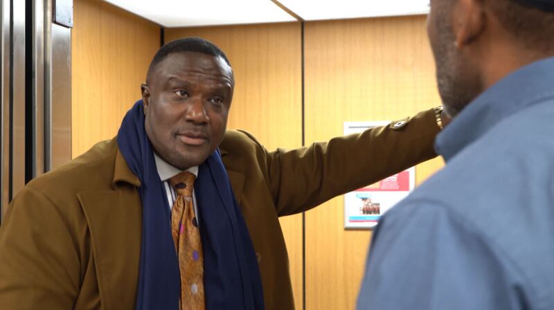 Joseph (Reginald Pelt) converses at the elevator with an employee at the fictional Metropolitan Building in downtown Metropolitan USA, in the GSW Network performance "Joseph Galilee."