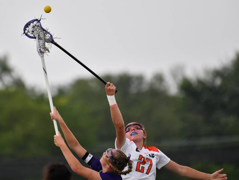 Crystal Lake’s Anna Starr (27) and Downers Grove North’s Ashley Poquette reach up for the ball after a face off during the Benet Supersectional game on June 3, 2025 at College of DuPage in Glen Ellyn.