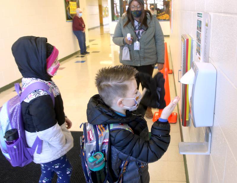 Gwendolyn Brooks Elementary School students use the hand sanitizer station before Shakyra Bomar, a resource assistant, takes their temperature as they enter the school for their first day of in-person classes Monday in DeKalb. School District 428 is using a hybrid schedule with some in-person classes and some families still choosing to learn remotely. Only students from kindergarten though second grade returned Monday with other grade levels returning soon.