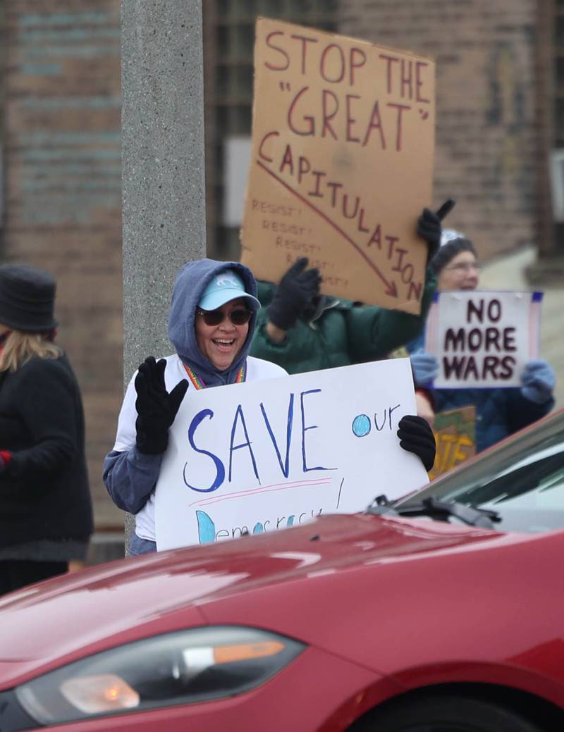 Protesters wave as cars honk in support Tuesday, Jan. 6, 2026, during a Venezuela Rapid Response Rally at Memorial Park on the corner of First Street and Lincoln Highway in DeKalb. The group gathered to voice their opposition to President Donald Trump and the administrations recent actions in Venezuela.