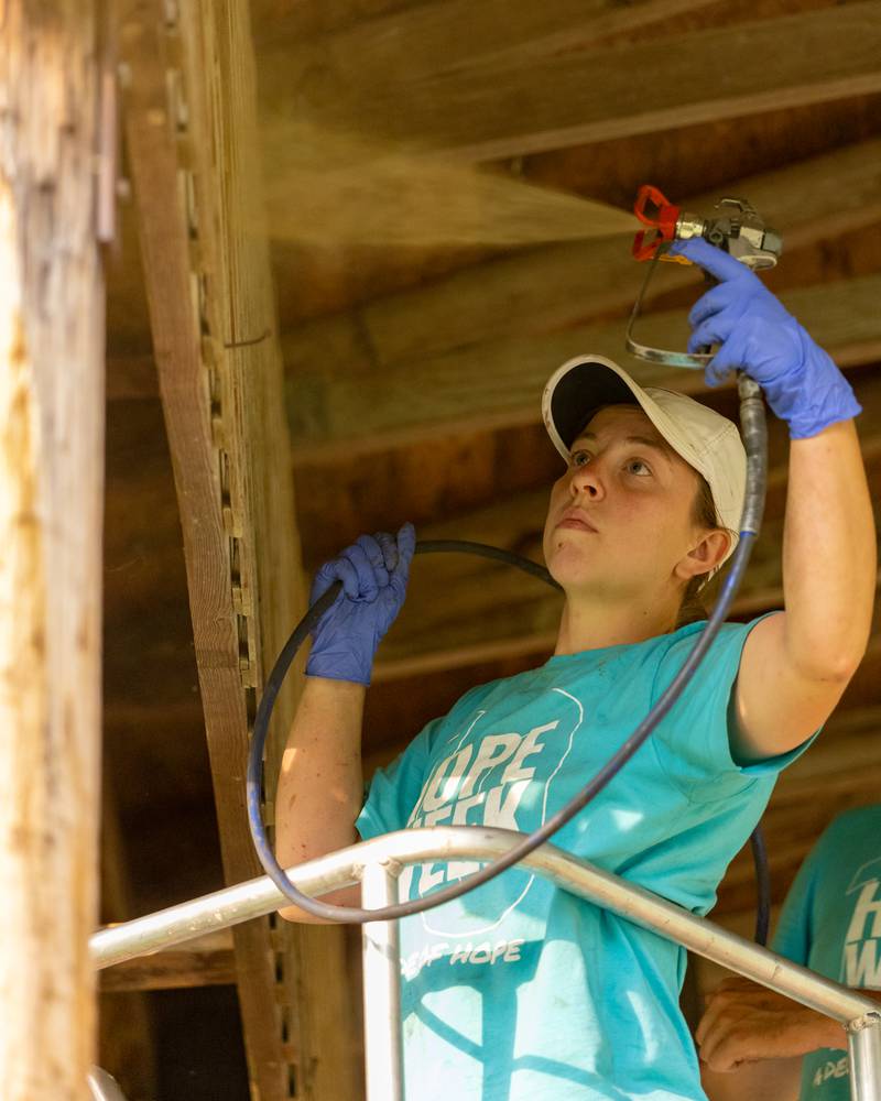 Cara Motter applies a stain with an applicator to the stage roof at Lehigh Park on June 5, 2025 in Oglesby.