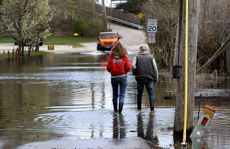 People walk and drive through flood waters on Bald Knob Road near the Bru Crew Bar and Grill  on Sunday, April 19, 2026, in Johnsburg as the Fox River continues to rise.