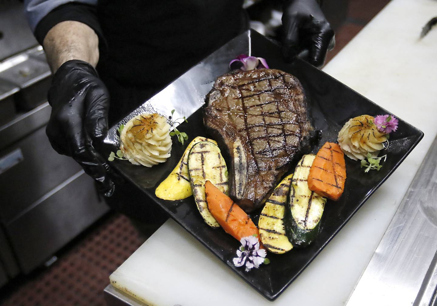 Executive chef Micheal Borlek with a bone-in-ribeye steak, with mashed potatoes, grilled carrots, squash, and zucchini, garnished with micro-greens and an orchid, on Tuesday, Jan. 14, 2025, at Addison’s Steakhouse, 335 Front St,,in McHenry,  The restaurant will be moving into the McHenry Country Club in March..