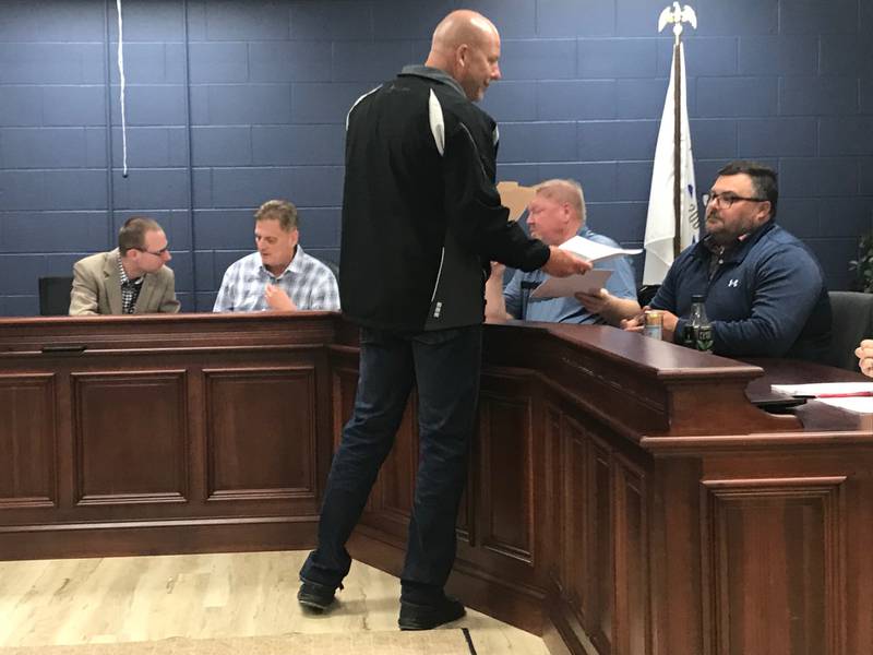 Cody Tucker (standing), plant manager of LaFarge, passes out pamphlets Wednesday to the Utica Village Board briefing trustees on recent blasting. LaFarge has installed monitoring equipment ahead of an April 20 blast, mindful of villagers' complaints about rattling windows and pictures blown off the walls.
